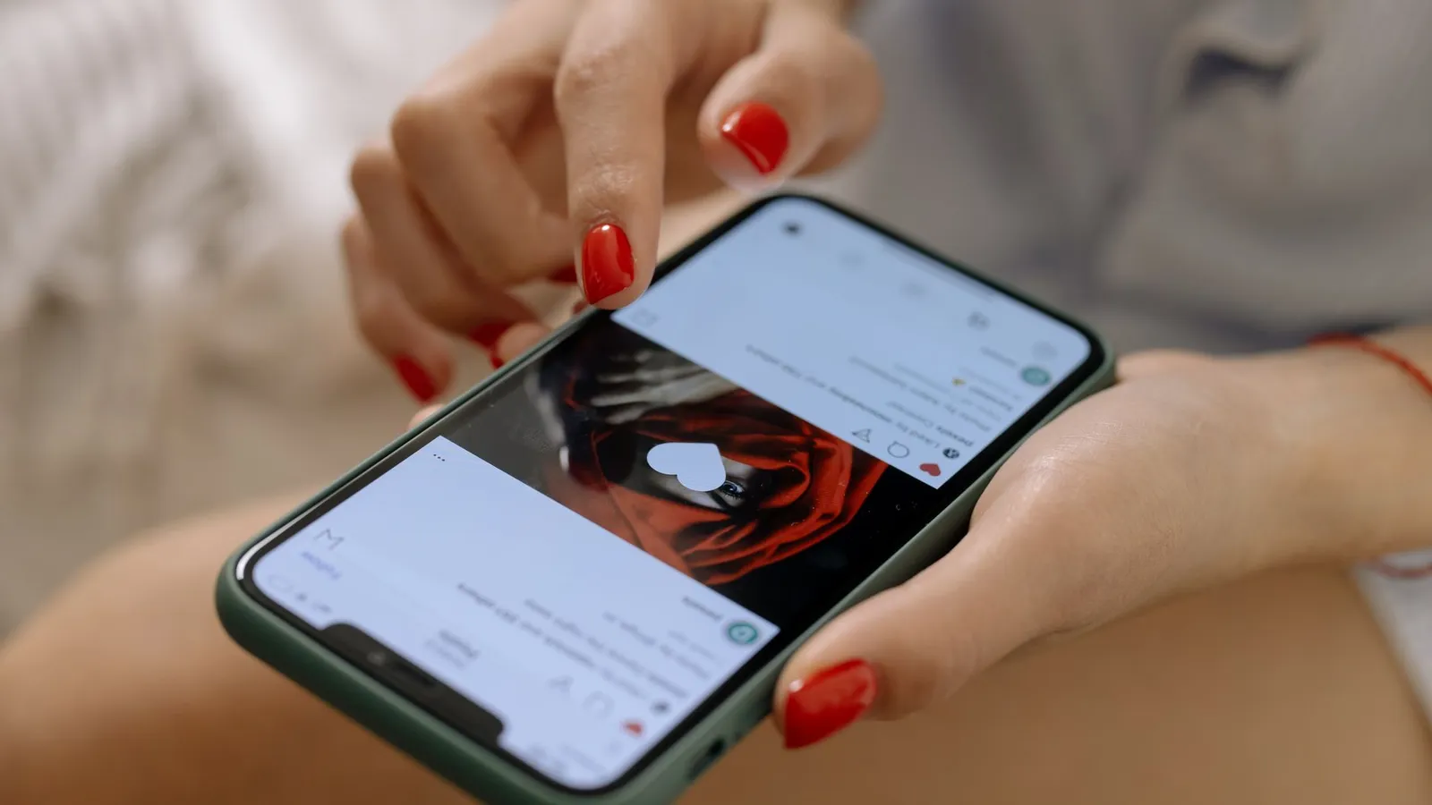 Close-up of a woman with red nails using a smartphone indoors, showcasing social media browsing.